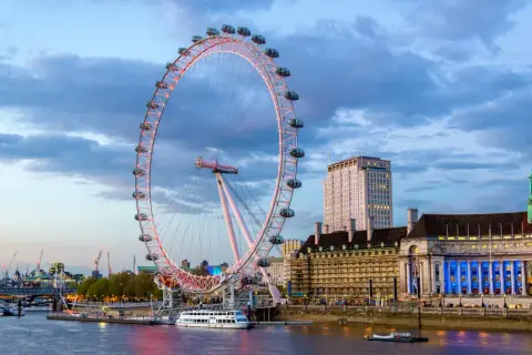 London Eye oświetlone wieczorem, z widokiem na Tamizę i budynki w tle.