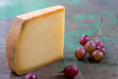 Un morceau de Comté aux cristaux savoureux, accompagné de grappes de raisins rouges sur un fond texturé.