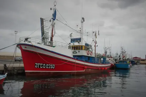 El barco museo de Burela, el "Reina del Carmen", luce su rojo y blanco vibrantes junto a otros pesqueros en un día nublado.