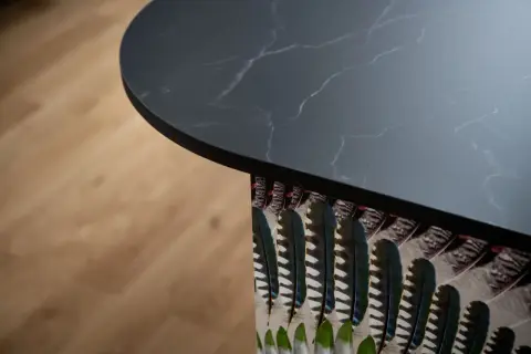 Plan de travail de cuisine en marbre noir avec un motif de plumes colorées sur le côté, créant une profondeur visuelle.