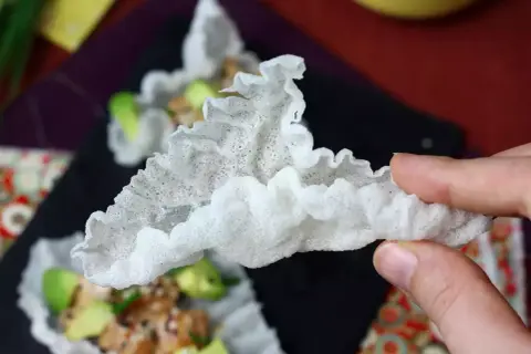 Chrupiące chipsy z papieru ryżowego, delikatnie pofałdowane, z widocznymi kawałkami awokado i mięsa w tle.