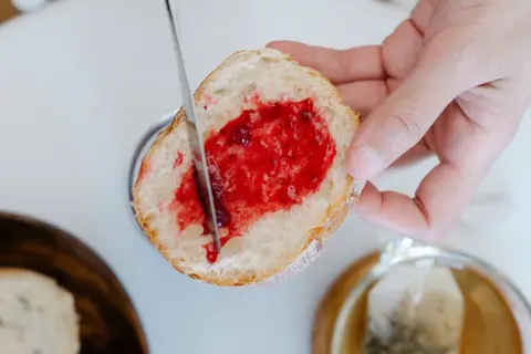 Ein Stück Brot wird mit Marmelade bestrichen, ein Genuss, der die Bedeutung eines Cheat Days unterstreicht.