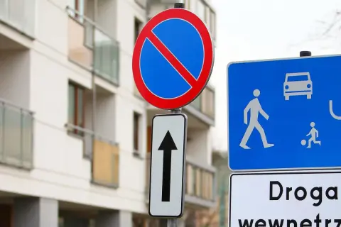 Znak b35 zakazu zatrzymywania się i postoju, obok znak drogi dla pieszych i rowerzystów, na tle nowoczesnego budynku.