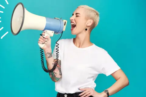 Mujer con pelo corto y tatuajes grita por un megáfono, mostrando el poder femenino.