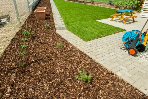 Gepflegter Garten mit frisch gemulchtem Beet, das trotz vereinzelten Unkräutern gut aussieht. Rasen mulchen ist hier die Devise.