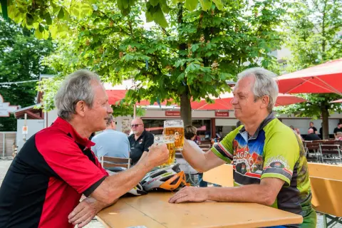 Zwei Radfahrer stoßen im Stadtbiergarten Schorndorf mit Bier an.