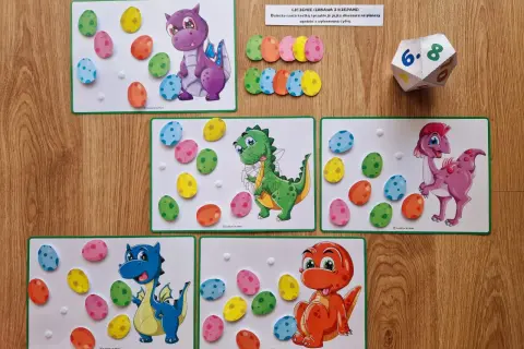 Zabawa edukacyjna na dzień dinozaura w przedszkolu: kolorowe jajka do przyklejania na planszach z dinozaurami.