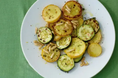 Zucchini gebraten italienisch mit Pinienkernen auf einem weißen Teller. Ein köstliches Gericht, das an einen sonnigen Tag in Italien erinnert.