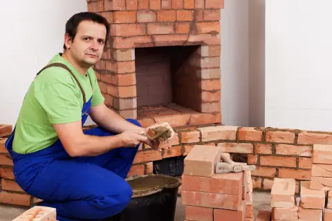 Murarz nakłada zaprawę na cegłę szamotową, budując kominek.