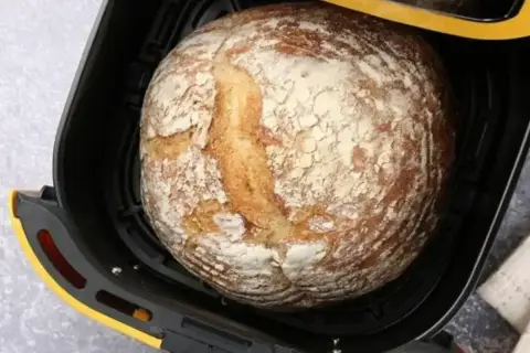 Chleb z airfryer, rumiany i lekko oprószony mąką, czeka na wyjęcie.