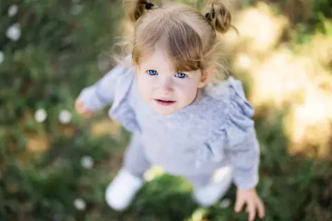 Un bébé aux yeux bleus vifs, coiffé de couettes, regarde vers le ciel. Le flouter arrière plan photo met en valeur son visage innocent.