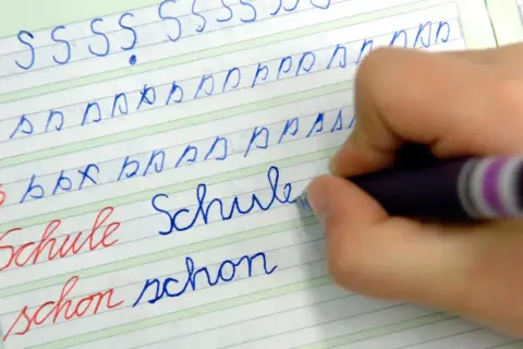 Kind übt das **Buchstaben schreiben lernen** auf liniiertem Papier. Es schreibt die Buchstaben S, b, p und die Wörter "Schule" und "schon".
