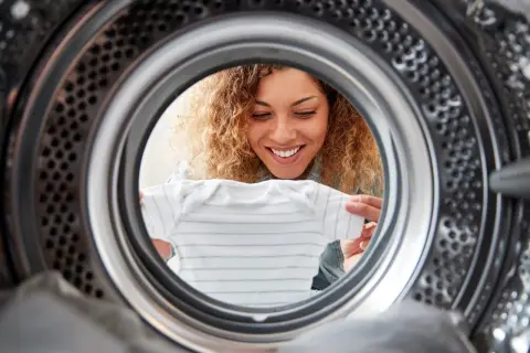 Uśmiechnięta kobieta wkłada ubranko do suszarki bębnowej Whirlpool.