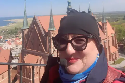 Kobieta w okularach i czapce na tle Fromborka. Wspaniałe widoki, idealne na rodzinne wycieczki i atrakcje dla dzieci.