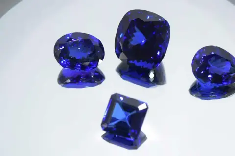 Cinco gemas de tanzanita piedra, de cortes y tamaños variados, brillan con un intenso color azul sobre un fondo reflectante.