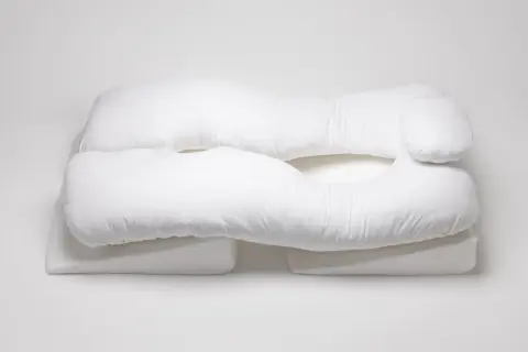 A white, U-shaped body pillow, designed for comfort and support, rests on wedge-shaped cushions. These almohadas ortopédicas offer a cozy embrace.