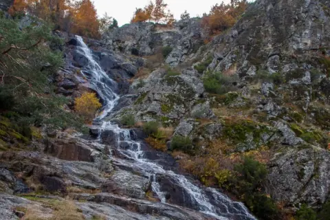 Cascada de Mojonavalle en otoño, con rocas cubiertas de musgo y árboles de hojas doradas.