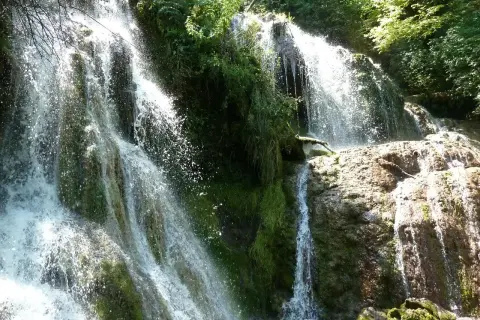 Cascada exuberante, ideal para saber qué visitar en Bulgaria. El agua cae sobre rocas cubiertas de musgo y vegetación frondosa.