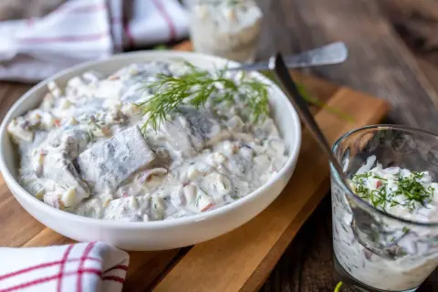 Kremowa, pyszna sałatka śledziowa z koperkiem i cebulką, podana w białej misie i szklance. Idealna na każdą okazję!