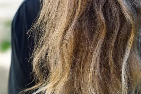 Chevelure châtain aux reflets blonds, légèrement ondulée, montrant l'effet de l'eau sur les cheveux.