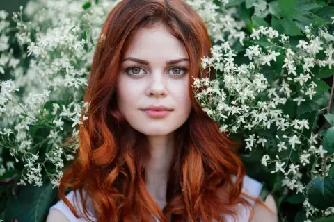 Eine Frau mit leuchtend roten, bunten Haaren blickt aus einem Meer von weißen Blüten.