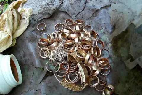 Kupa złotych pierścionków i biżuterii na ziemi, obok białego pojemnika i materiału.