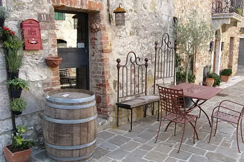 Un angolo pittoresco nella regione del Chianti con un barile di legno, piante aromatiche, un tavolino da esterno e un vecchio cancello in ferro battuto.