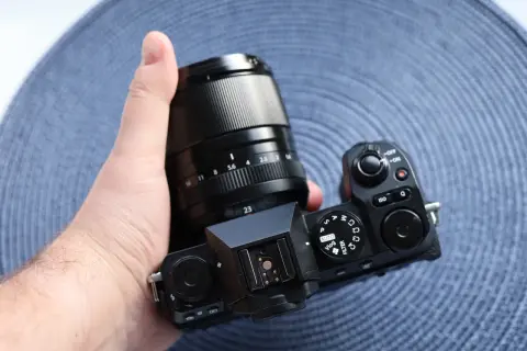Dłoń trzyma aparat Fujifilm X-S20 z obiektywem. Widoczne pokrętła trybów i przyciski.