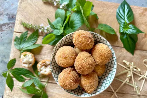 Goldbraune Arancini, frisch zubereitet nach einem tollen arancini rezept, liegen in einer Schale. Frische Kräuter und Holzspieße zieren die Holzplatte.