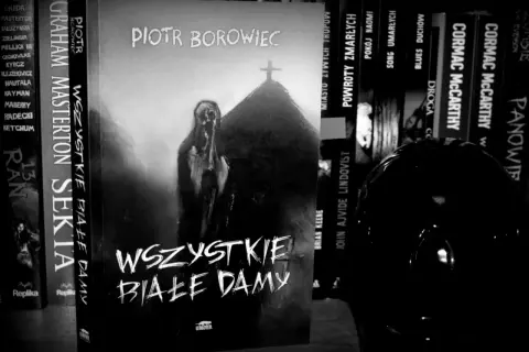 Czarno-biała okładka książki "Wszystkie białe damy" Piotra Borowca z postacią i krzyżem.