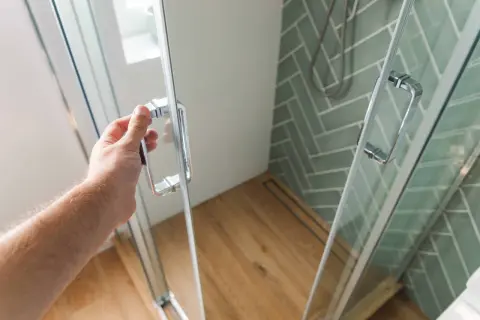 Ręka otwiera drzwi kabiny prysznicowej. Zastanawiasz się, czym umyć kabinę prysznicową z pleksi, by lśniła czystością?