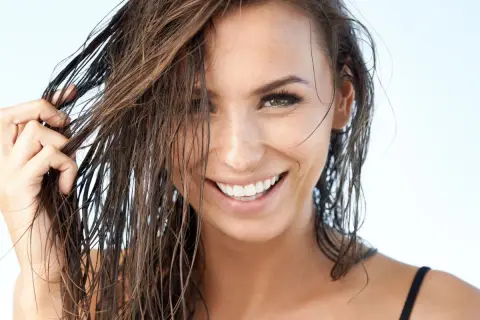 Mujer sonríe con pelo efecto mojado, luciendo su cabello castaño oscuro y húmedo.