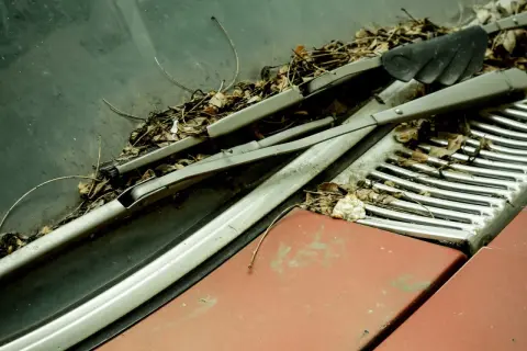Zarośnięty liśćmi mechanizm wycieraczek Astra G, zardzewiałe ramiona i zniszczona maska sugerują długie zapomnienie.