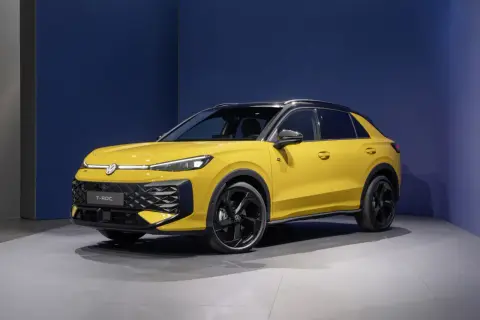 Żółty Volkswagen T-Roc VW z czarnym dachem i felgami stoi na szarej podłodze przed niebieską ścianą.