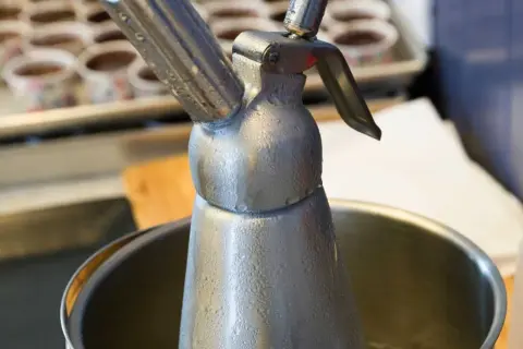 Metalowy syfon do bitej śmietany, pokryty kroplami kondensatu. Zastanawiasz się, ile może stać w lodówce?