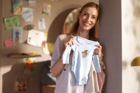 Glad mamma visar upp en ljusblå babybody med ett gulligt ekollonmotiv. Hon är veckans babe och ser fram emot att klä sin lilla skatt.