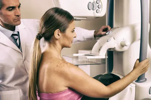 Lekarz nadzoruje badanie mammograficzne, które może być wstępem do biopsji gruboigłowej. Kobieta przygotowuje się do procedury.