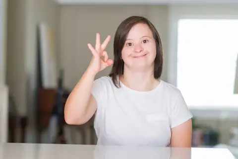 Ragazza con sindrome di down sorride e fa il segno "ok" con la mano.