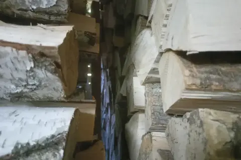 Stos drewna opałowego, z widocznym układaniem drewna korą do góry, tworzy wąskie przejście.