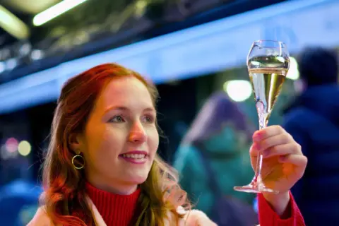 Frau mit roten Haaren hebt ein Glas Sekt, das auf der Hefe gereift ist, in festlicher Beleuchtung.