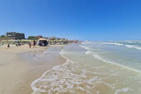 Spiaggia affollata a Senigallia mare, con ombrelloni, lettini, bancarelle e gente che passeggia. Il mare azzurro e calmo invita a un tuffo.