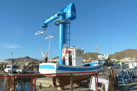 Barco pesquero blanco y azul en dique seco, bajo una grúa azul con "C.N. San José" escrito.