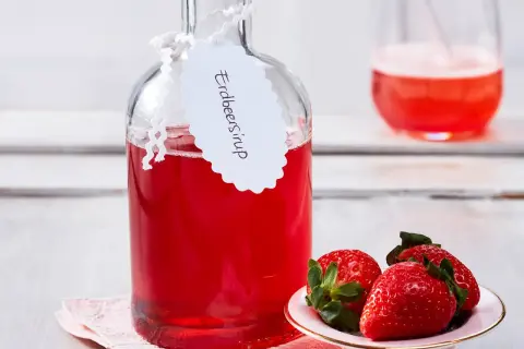 Flasche mit selbstgemachtem Erdbeersirup, garniert mit frischen Erdbeeren. Perfekt für Cocktails oder als Topping.