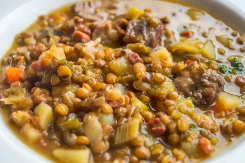 Un plato reconfortante de lentejas con trocitos de sobrasada, patatas y verduras en un caldo sabroso.