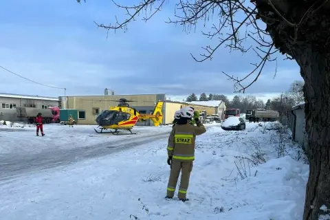 Śnieg, śmigłowiec ratunkowy i strażak na tle budynków. Sytuacja wygląda na izolowane zdarzenie medyczne.