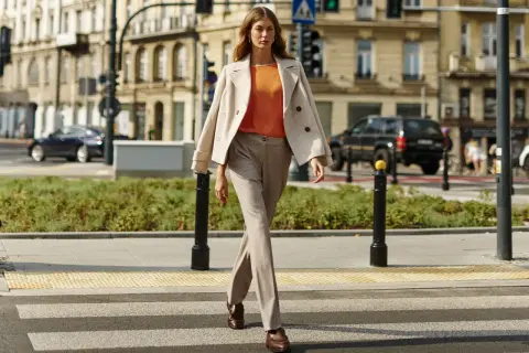Elegancka kobieta prezentuje stylizacje do beżowego płaszcza, idąc przez pasy.