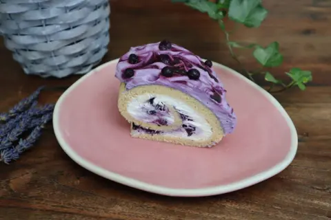 Roulé moelleux garni de crème chantilly mascarpone et myrtilles, nappé d'une crème violette aux fruits.