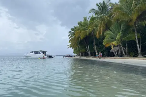 Rajska plaża na San Blas z palmami, łodzią i ludźmi kąpiącymi się w turkusowej wodzie.