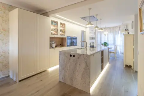 Cocina moderna con isla central de granito, gabinetes blancos y suelo de madera. Una guía visual sobre como distribuir una cocina funcional y elegante.