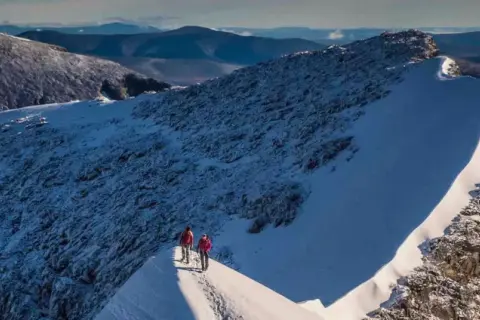 Två vandrare på en snöig bergskam med Kebnekaise i bakgrunden. En bra kebnekaise packlista är avgörande för en säker tur.